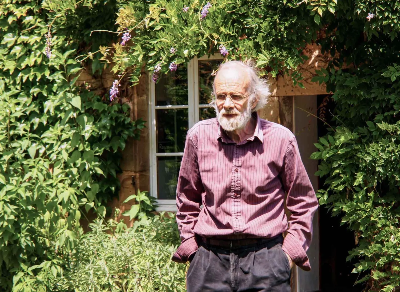 Homme âgé barbu devant une maison fleurie