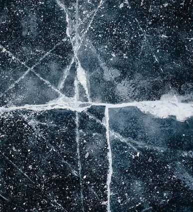 Surface de glace sombre parcourue de fissures blanches